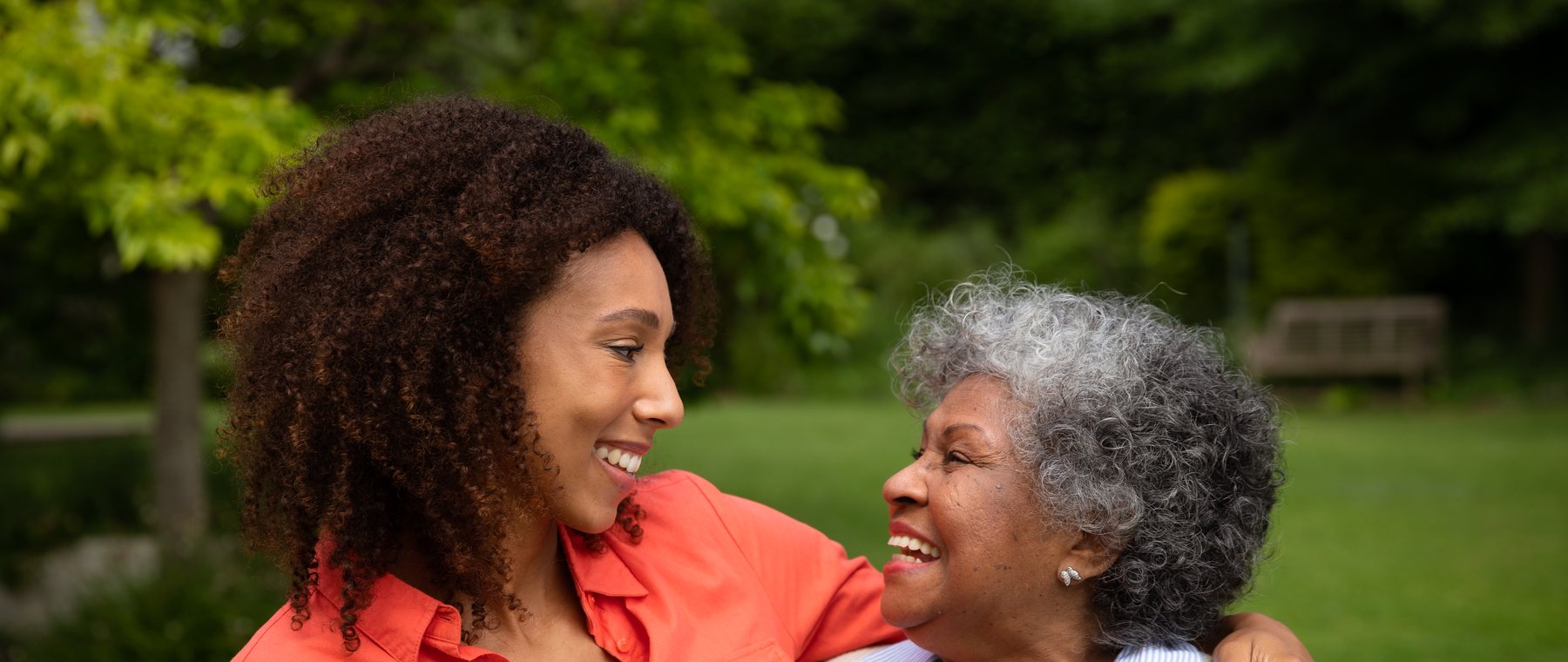 A daughter and her mother smiling at each other in the garden