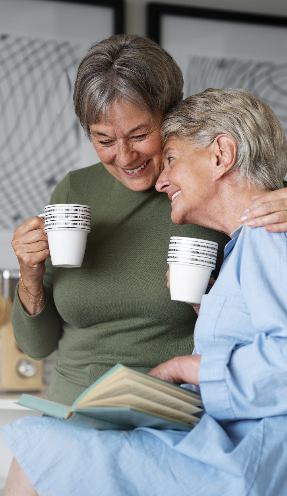 Two residents sharing tea and a book, one with an arm around the other