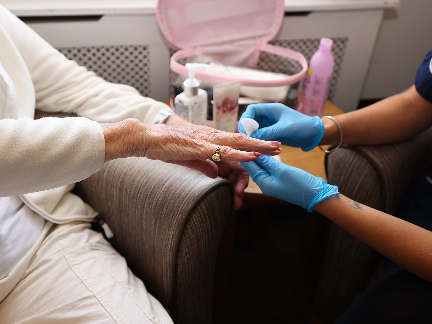 A carer in gloves gently holding a resident's hand while doing her nails