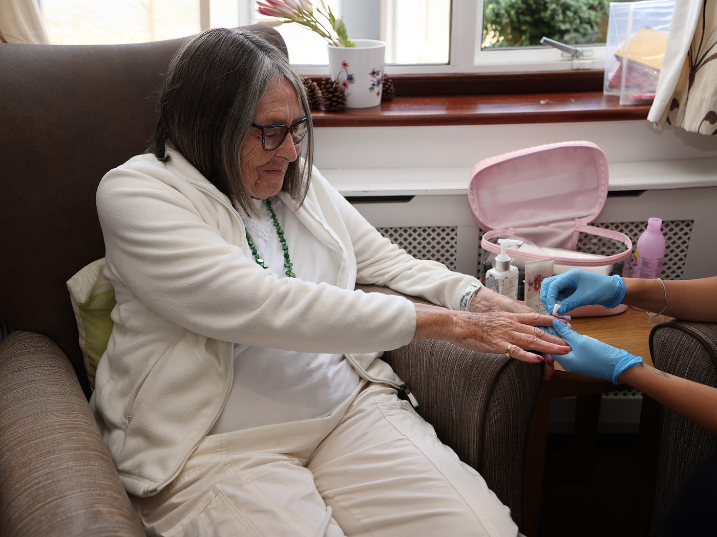 A carer doing a resident's nails as she sits in her armchair