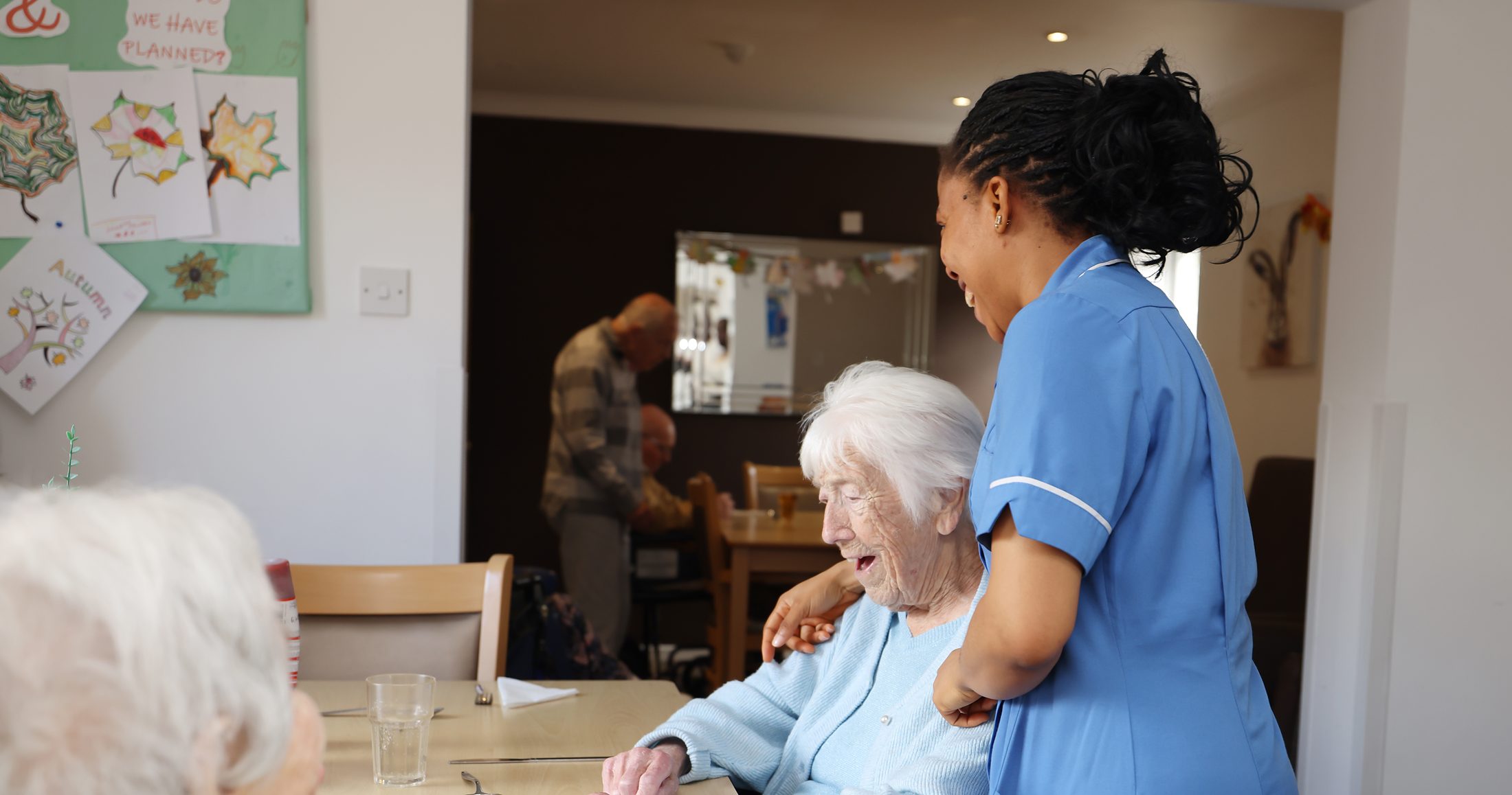 A resident laughing on the garden bench in the sunshine, a visitor's hand resting on her shoulder