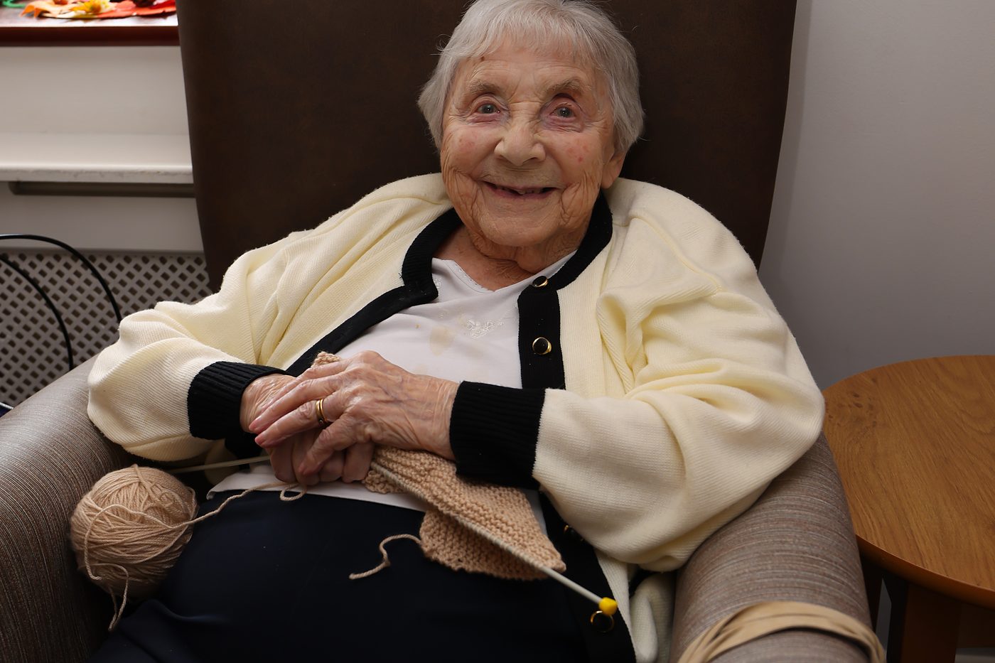 A resident smiling in her armchair with her knitting on her lap