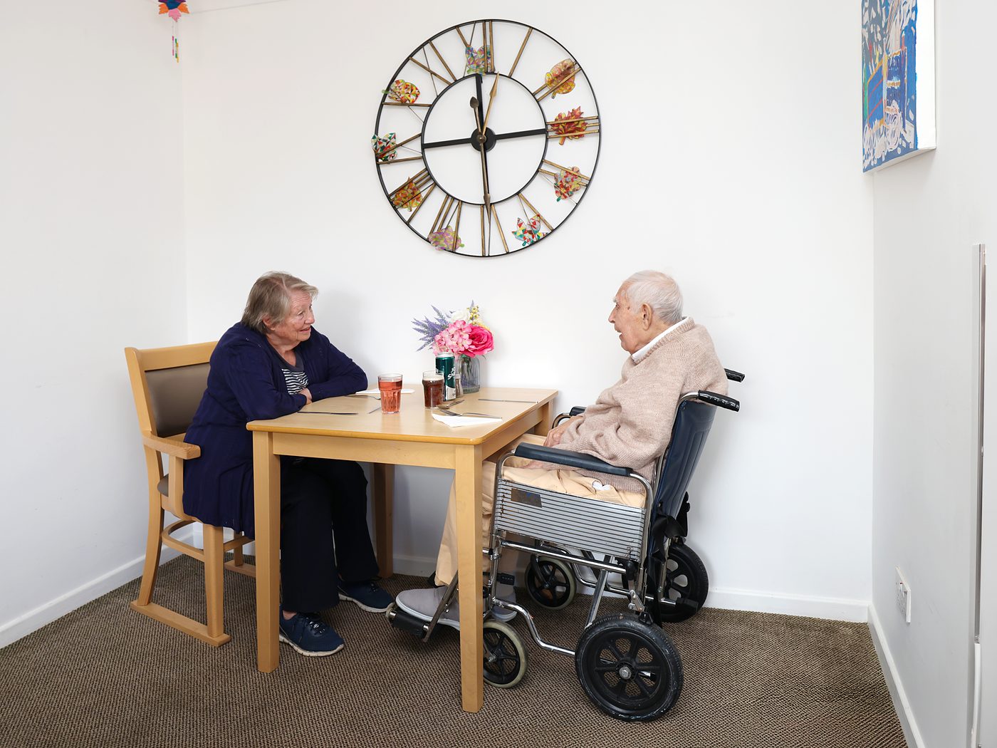A resident and a family member chatting over a drink at a table in the home